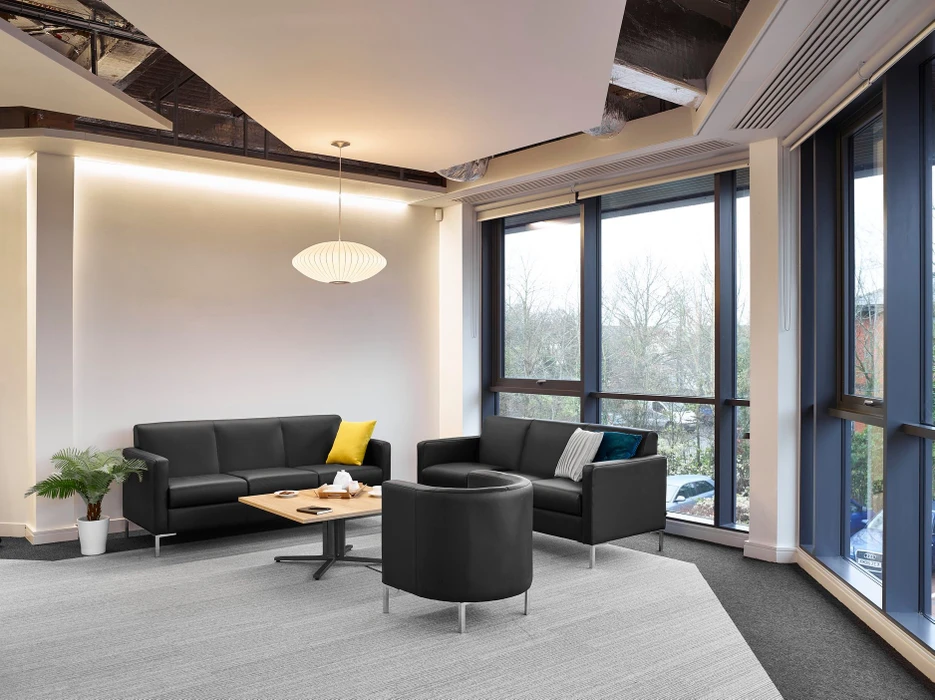Espace de travail open space moderne aux murs bleus, avec postes de travail en bench configurés en îlots, équipés de moniteurs, laptops et cloisons acoustiques grises